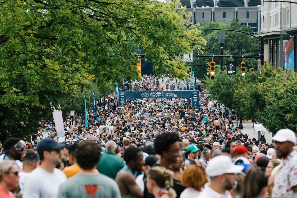 Hundreds of runners the finish line of a race in a street with green trees on both sides