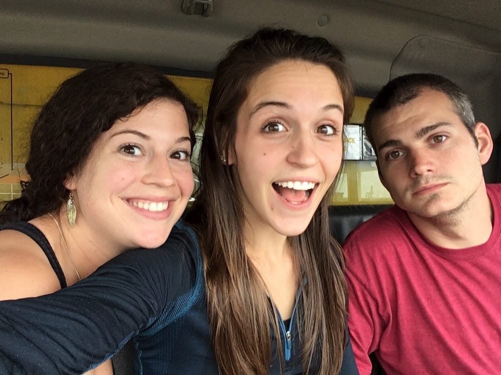 Two women and a man sitting inside a car smiling for the camera