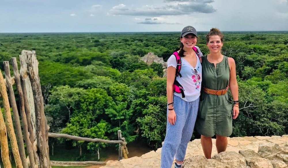 Two women standing together above a rainforest with green trees