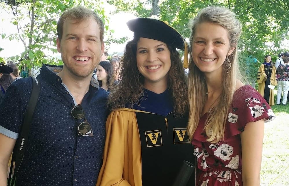 A man and a women on either side of another women in cap and gown outside during a graduation