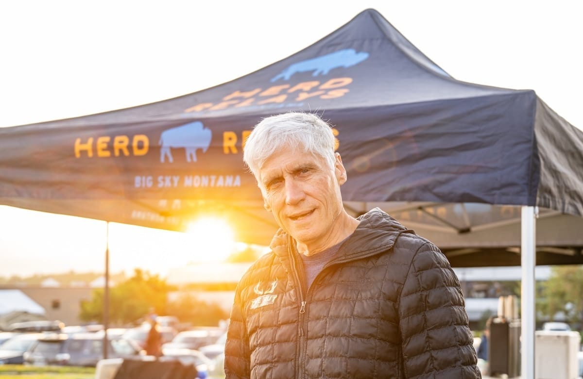 A man in a black jacket standing outside in front of a pop-up tent for a trail race