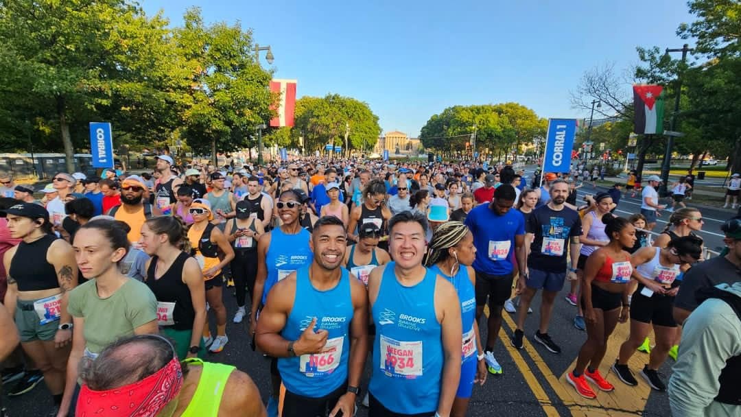 Two male runners smiling at the start of a race surrounded by other runners with a blue sky in the background