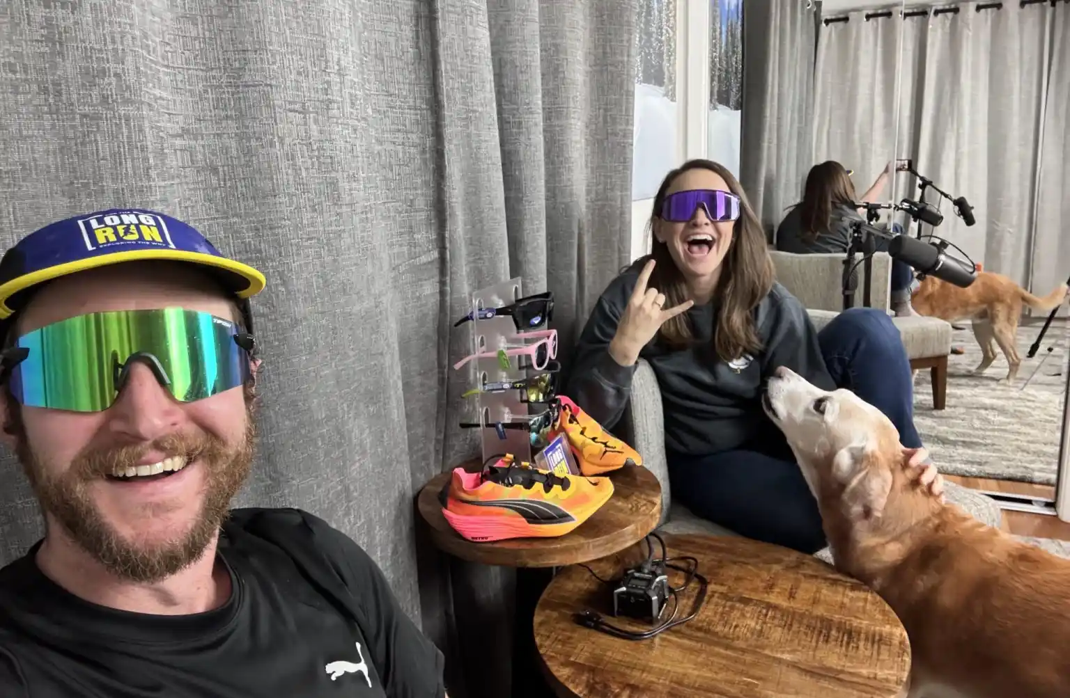 A man and a woman in sunglasses smiling for a selfie while sitting inside on opposite sides of a small table