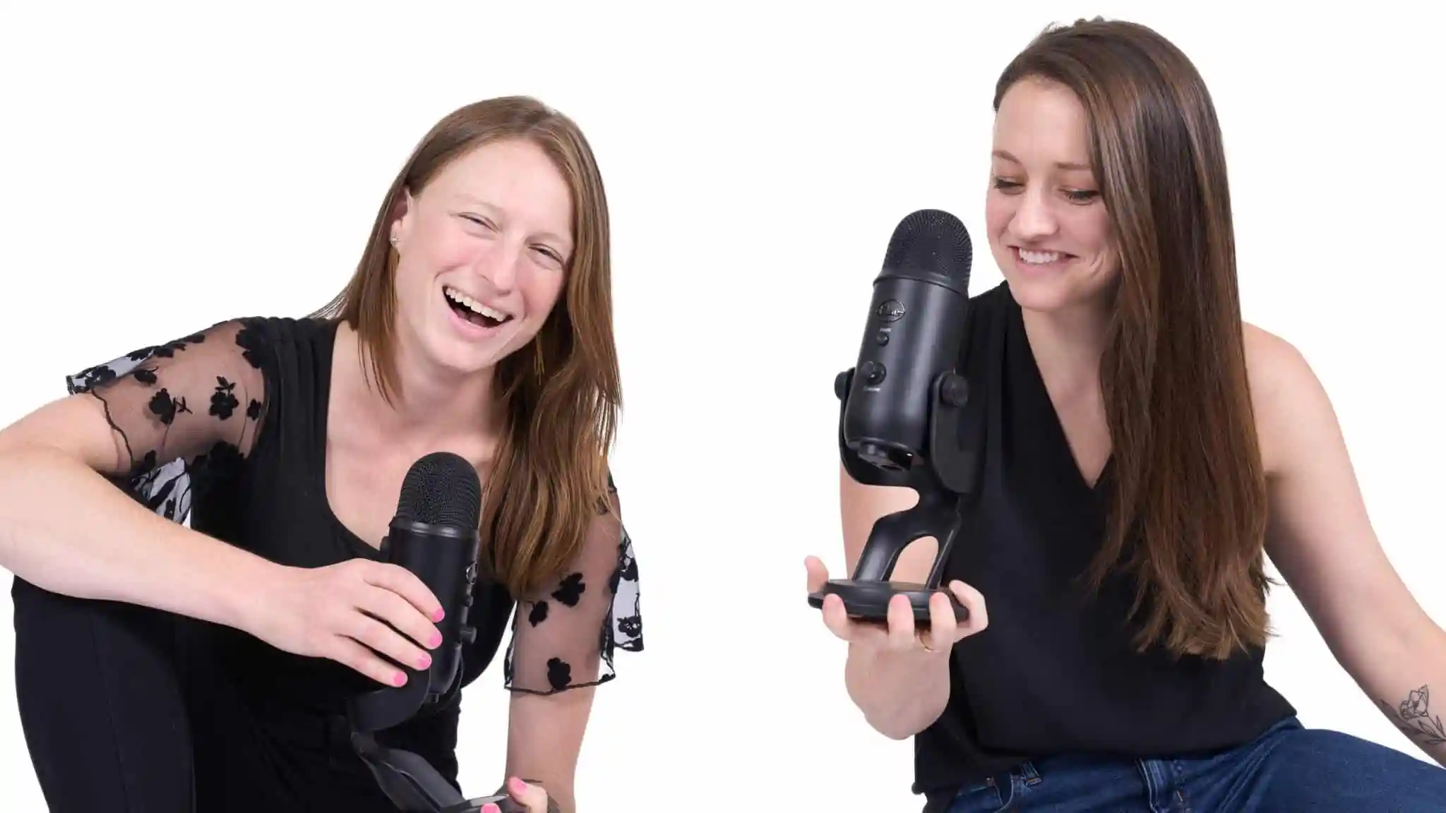Two women in black shirts laughing and holding podcast microphones