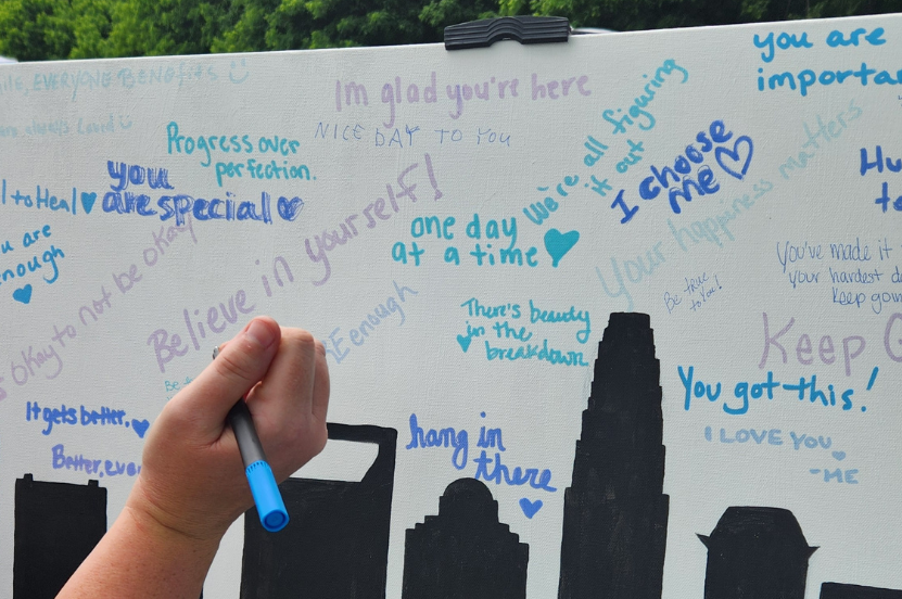 A person holding a pen and signing a white board with other signatures on it and an image of the the Charlotte city skyline 