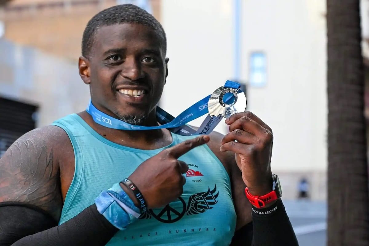 A man in a turquoise tank top posing for a photo holding a race medal