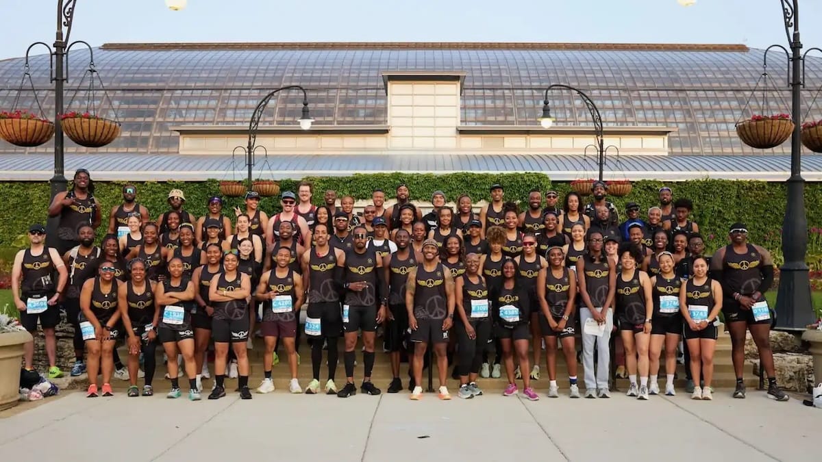 A large group of runners wearing black shorts and shirts posing outside in front of a building for a group photo