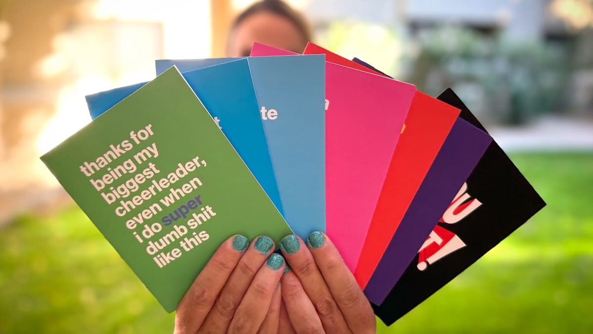 A person holding a set of colorful greeting cards fanned out in front of their face