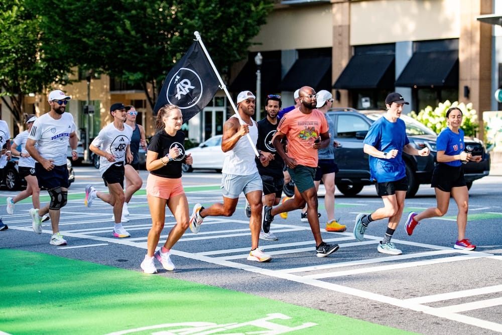 A group of runners running down a street with one runner holding a flag