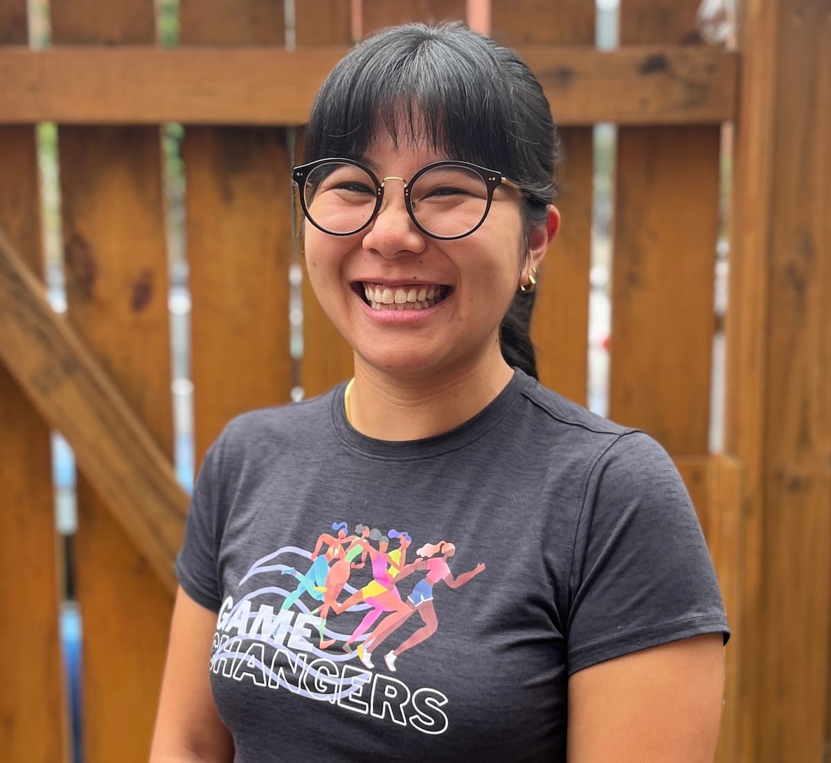 A woman smiling, posing for a photo in front of a brown fence