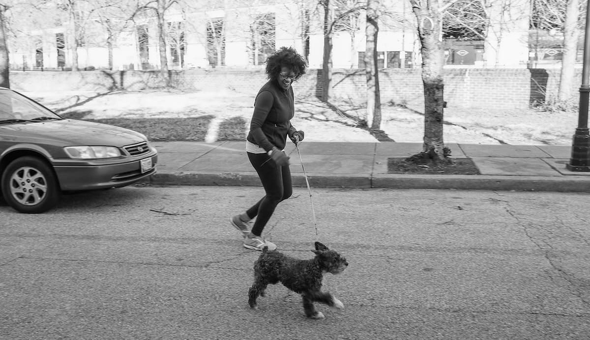 A woman running down a city street alongside a small dog