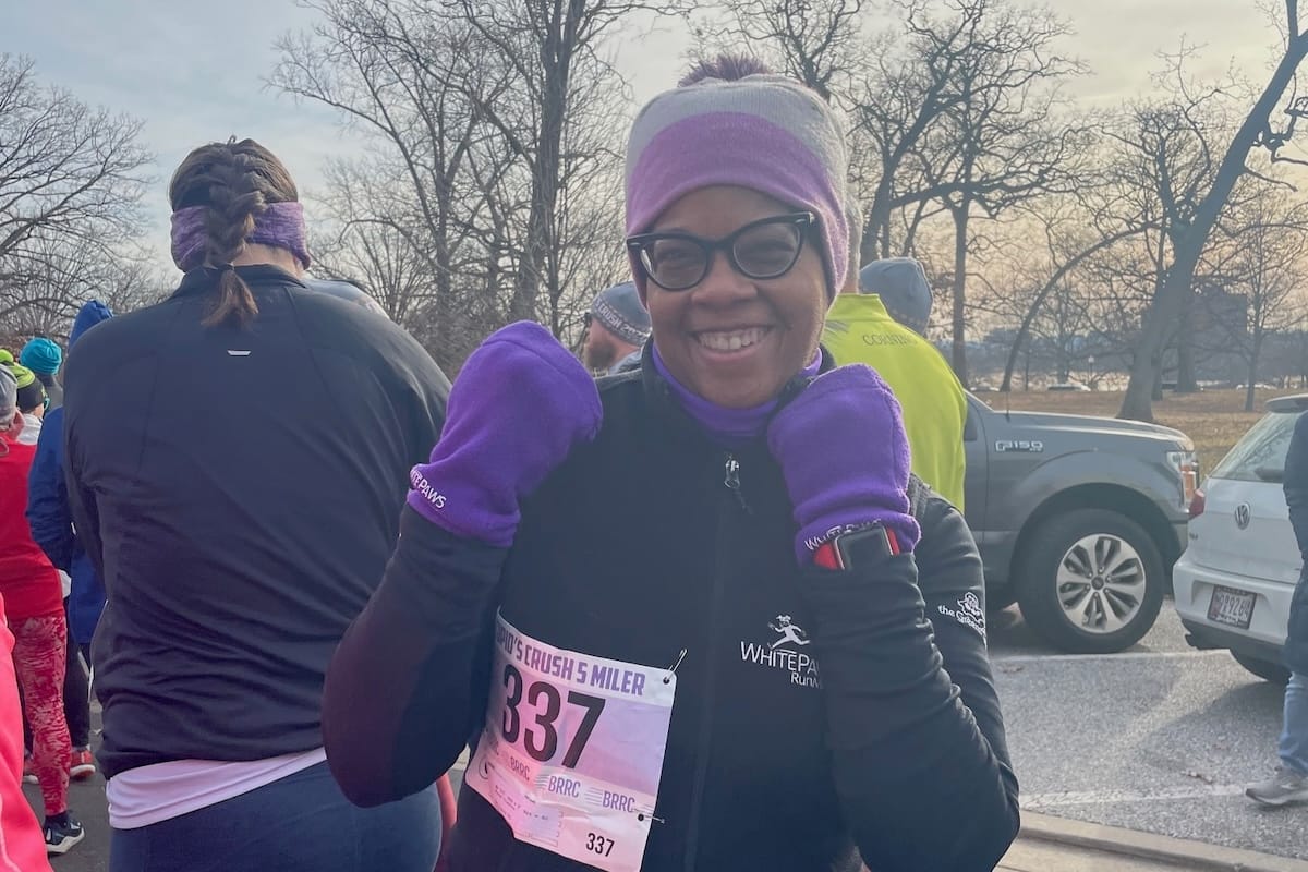 A woman outside wearing cold weather running gear and holding her hands up in a boxing stance with purple mittens on
