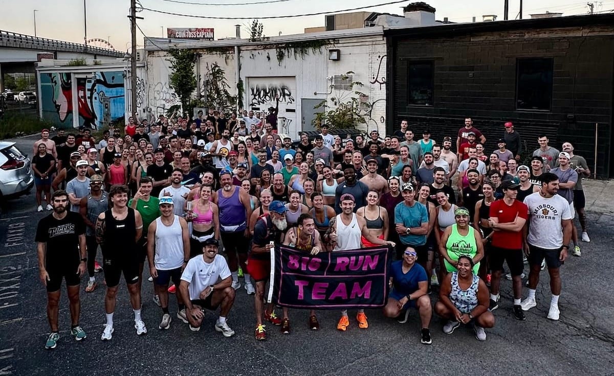 A large group of runners in a downtown area behind a building posing for a group photo