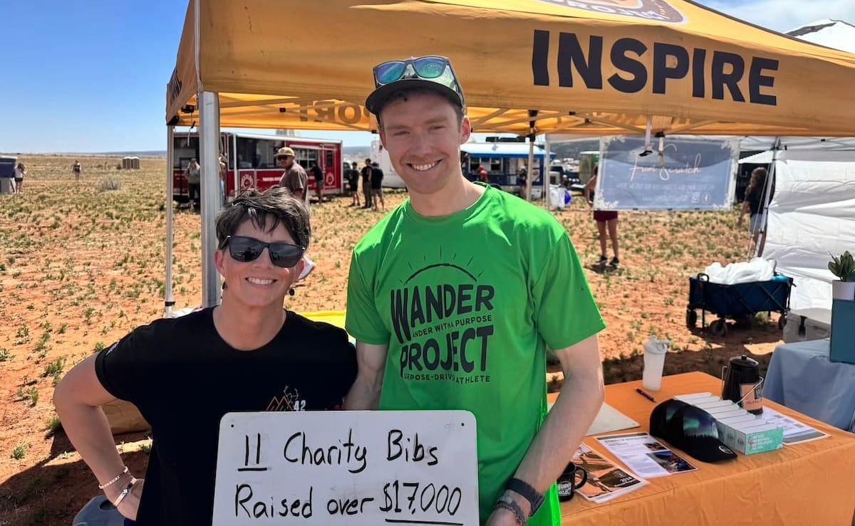 Two people standing under a yellow tent outside in a desert and holding a white sign that reads "11 charity bibs raised over $17,000"