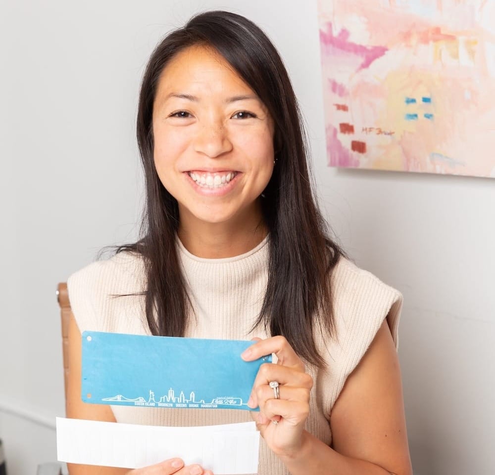 A woman sitting at a table and posing while holding a name bib for running races