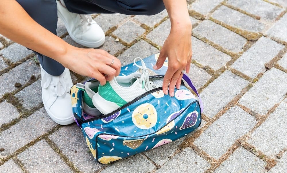 A person crouching on the ground outside pulling a shoe out of a shoe bag decorated with illustrated donuts