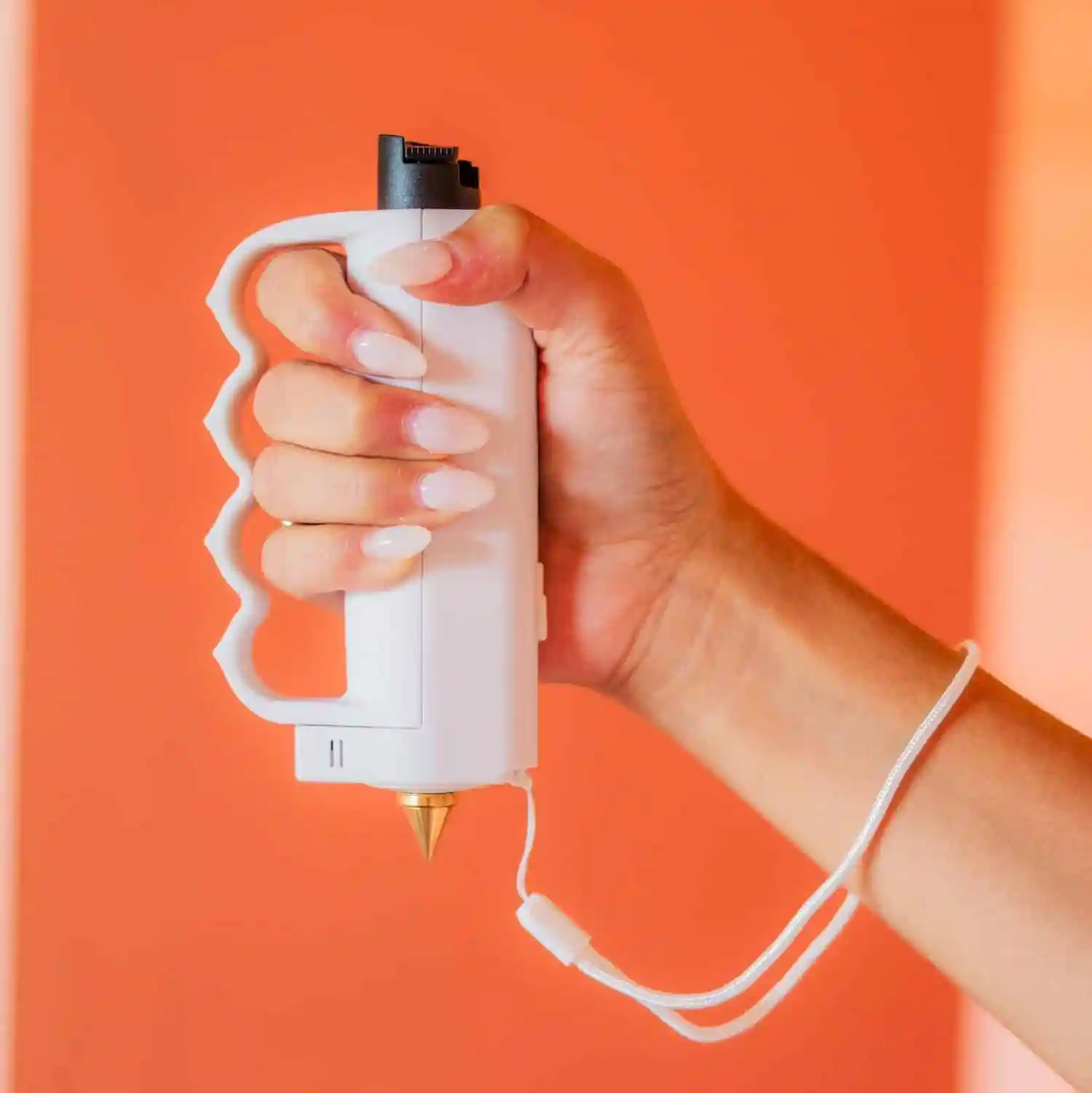 An arm extended with a hand holding a pink pepper spray device