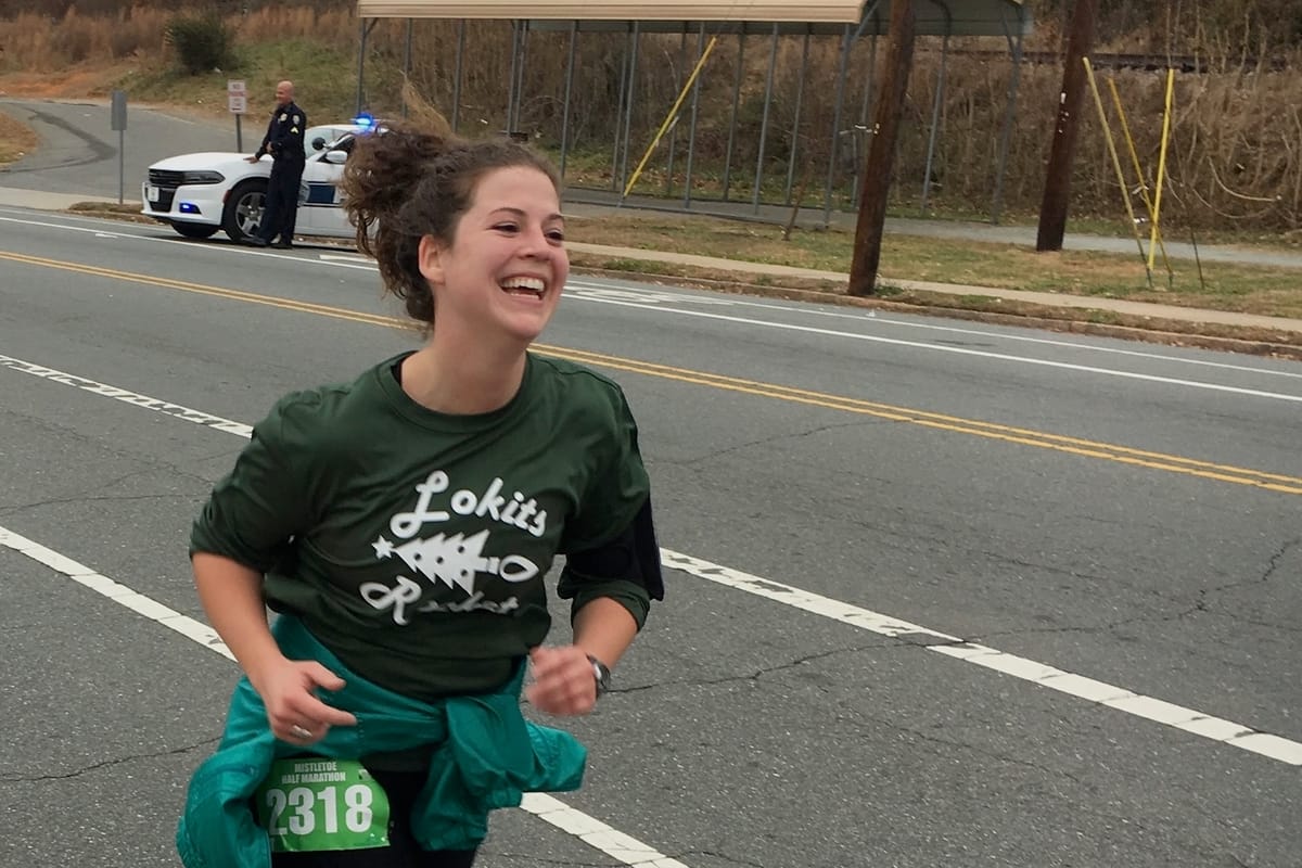 A woman smiling while running down a street during a road race