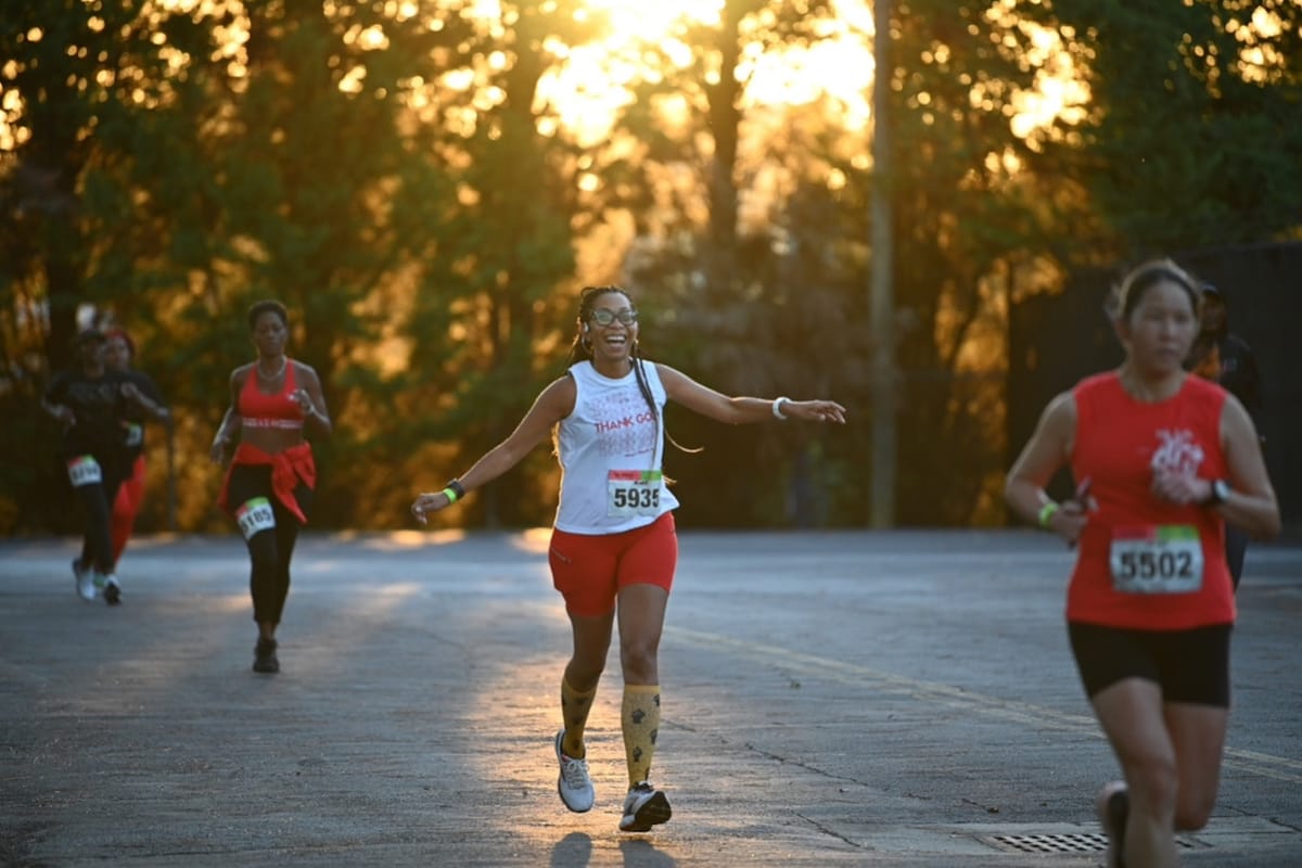 Several women running in a race on a paved road with trees in the background