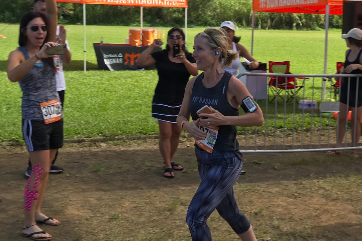 A female runner running along a dirt path with several females cheering fo