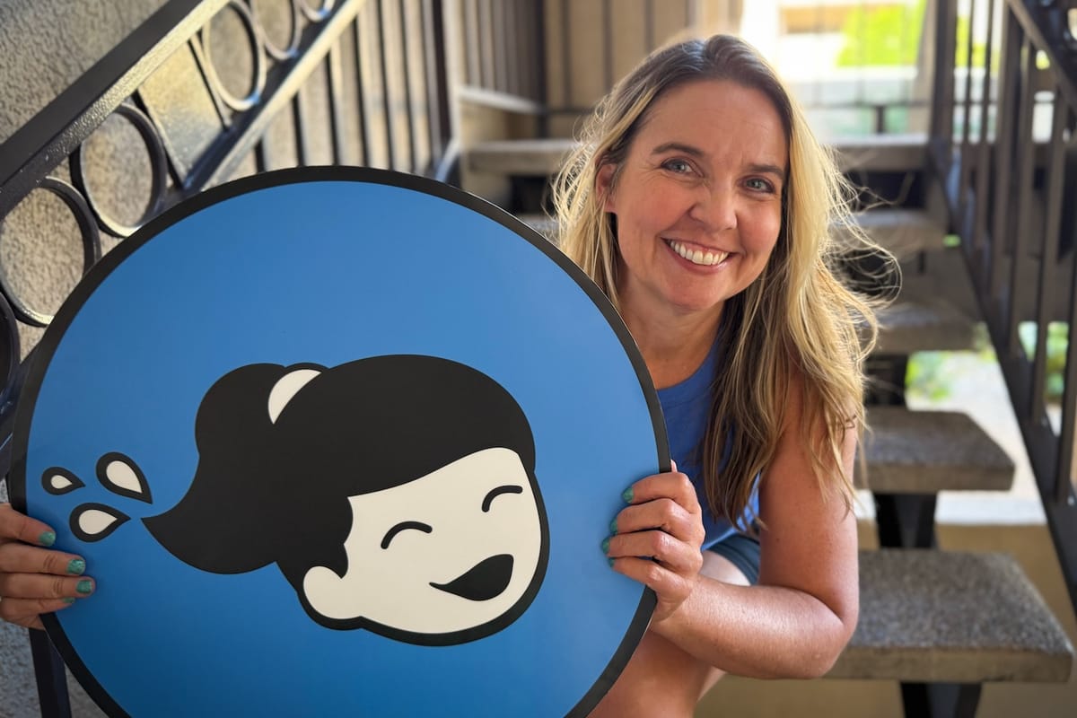 A woman sitting outside on a staircase holding a large, round blue poster with a logo on it