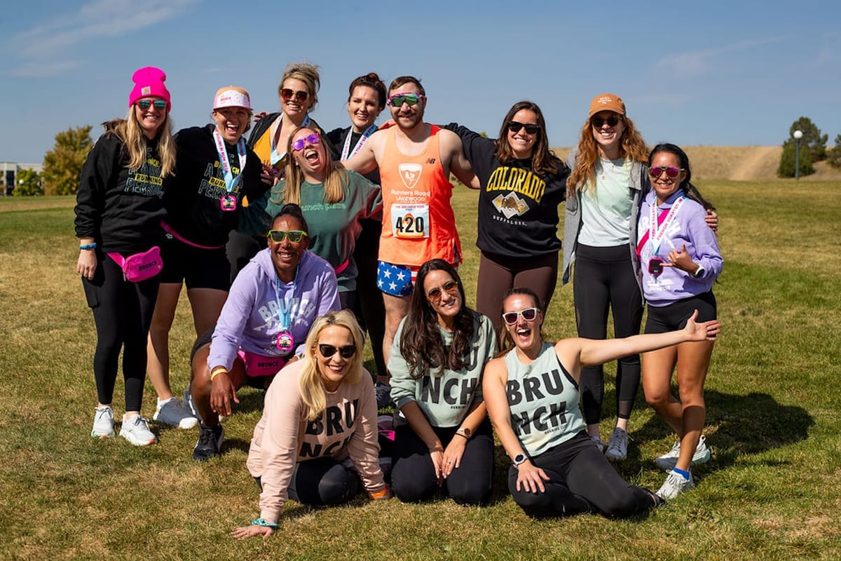A group of runners posing for a photo on green grass with a blue sky in the background and everyone looking excited 