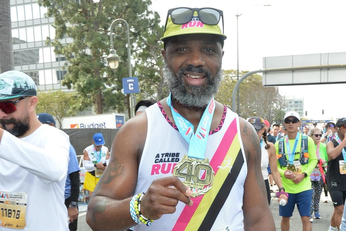 A man in a racing jersey and yellow hat posing for a photo and holding a race medal