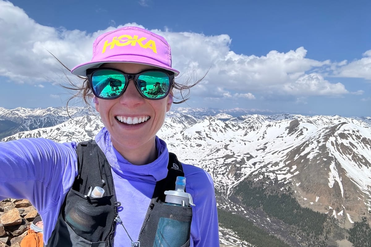 A woman taking a selfie at the top of a mountain with snow-covered mountains in the background
