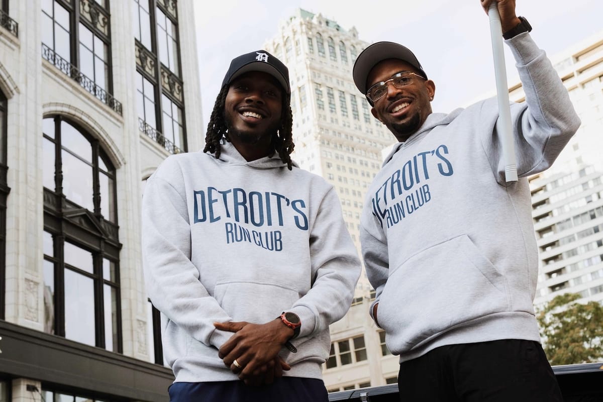 Two men in white sweatshirts and black hats, posing for a photo in front of city buildings