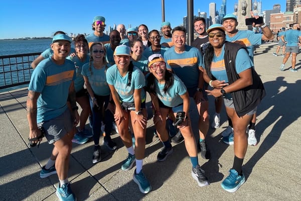 A group of people posing for a photo, all wearing turquoise shirts and standing on a boardwalk with water and a blue sky in the background
