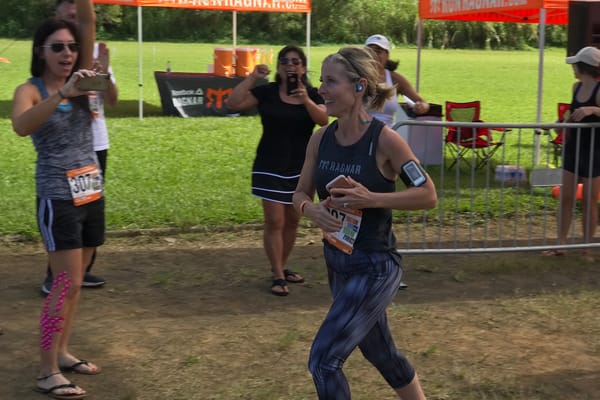 A female runner running along a dirt path with several females cheering fo