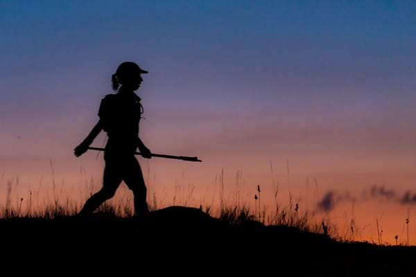 The silhouette of a woman walking outdoors along a trail at sunset