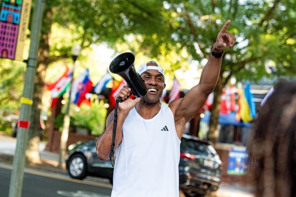 A man holding a megaphone in one hand and raising his other hand outside on a street