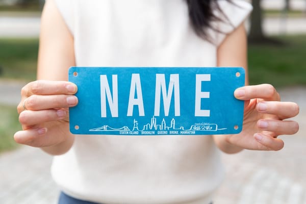 A woman holding out to the camera a blue bib with white lettering 